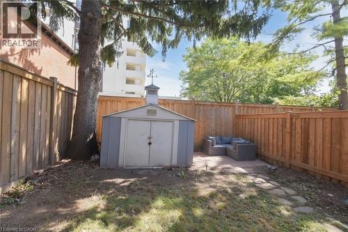 Fenced yard featuring a metal storage shed, mature trees, and a paver patio - 35 Tisdale Street S, Hamilton, ON 
