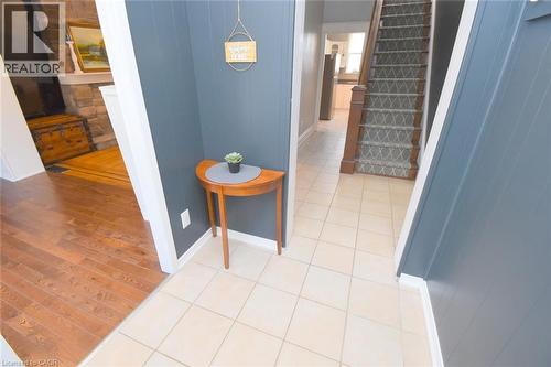 Tiled flooring entry with a wood-finish staircase featuring a patterned runner and dark wood newel post - 35 Tisdale Street S, Hamilton, ON 