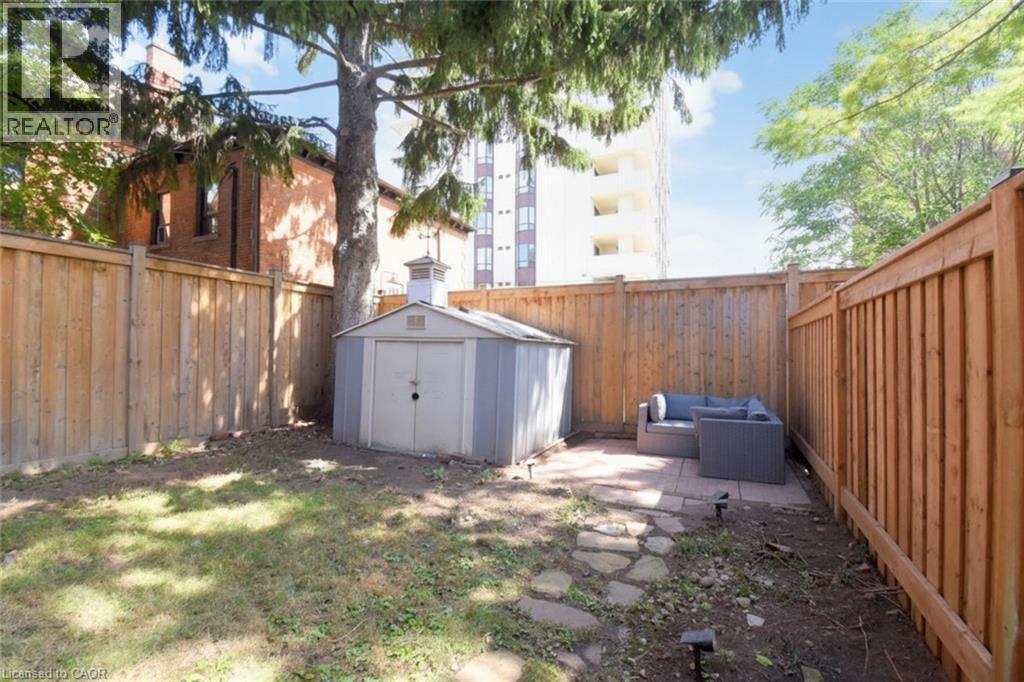 Fenced rear yard featuring a paved patio area, stone pathway, and a storage shed - 35 Tisdale Street S, Hamilton, ON