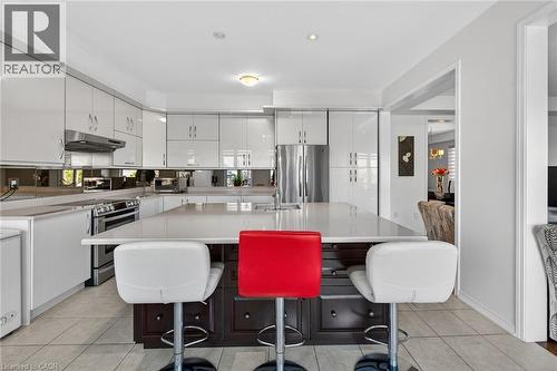 Kitchen with a kitchen island with sink, stainless steel appliances, two tone color scheme, a breakfast bar area, and light tile patterned floors - 97 Sirente Drive, Hamilton, ON 