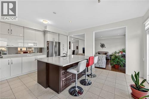 Dual tone kitchen with dual tone cabinetry, freestanding refrigerator, a kitchen bar, an island with sink, and light tile patterned floors - 97 Sirente Drive, Hamilton, ON 