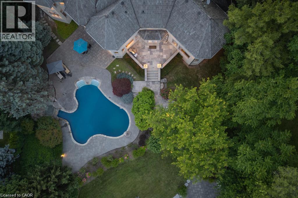 Property featuring a curvilinear swimming pool, extensive stone patio, mature landscaping, and multi-level outdoor entertaining areas - 4038 Lakeshore Road, Burlington, ON
