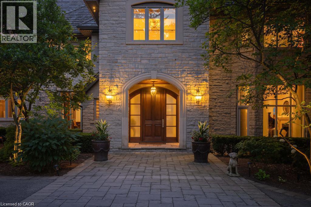 Stone exterior facade with a prominent arched entry, wood-paneled double doors, and decorative outdoor lighting - 4038 Lakeshore Road, Burlington, ON