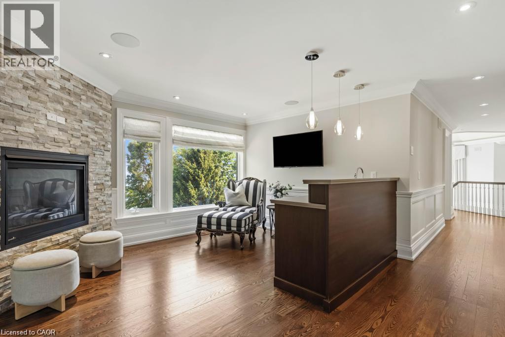 Wood-finish flooring, stone-clad fireplace, large windows, custom wet bar, and overhead pendant lighting - 4038 Lakeshore Road, Burlington, ON