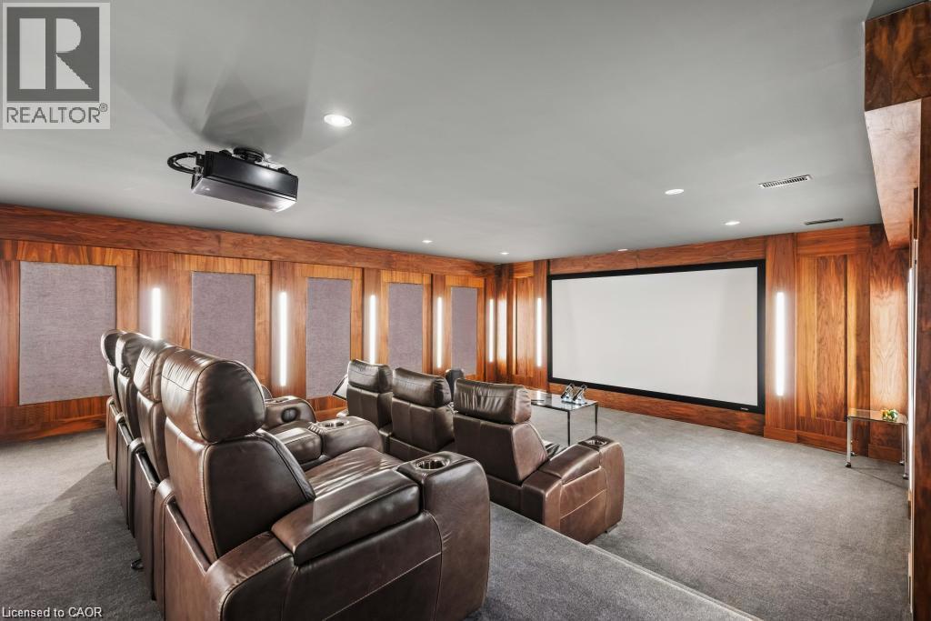 Dedicated media room featuring wood paneling, a large projection screen, integrated projector, and recessed lighting - 4038 Lakeshore Road, Burlington, ON