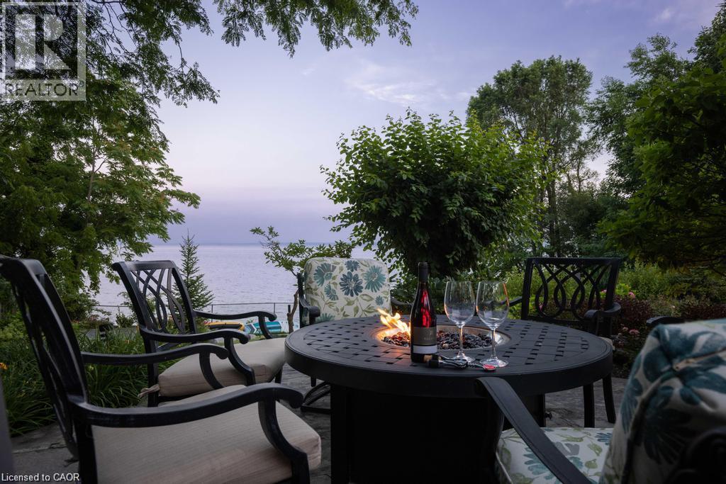 Paved patio with a built-in fire pit and surrounding mature trees - 4038 Lakeshore Road, Burlington, ON