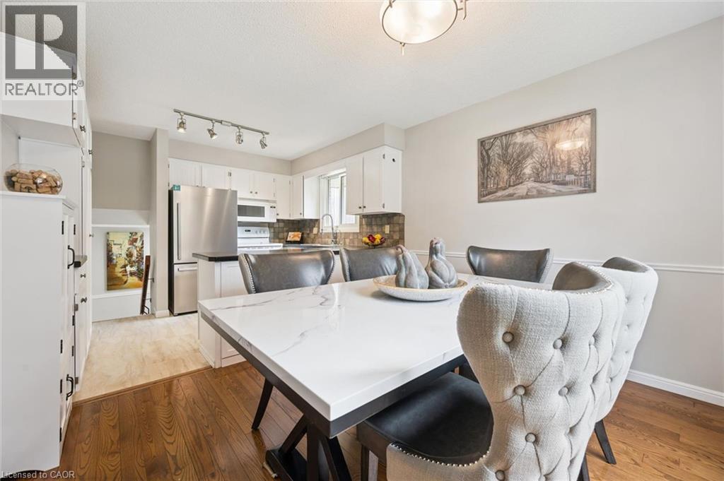 Rich wood-finish flooring, white built-in cabinetry, stainless steel appliances, dark countertops, and a track lighting fixture - 21 Colebrook Court, Kitchener, ON