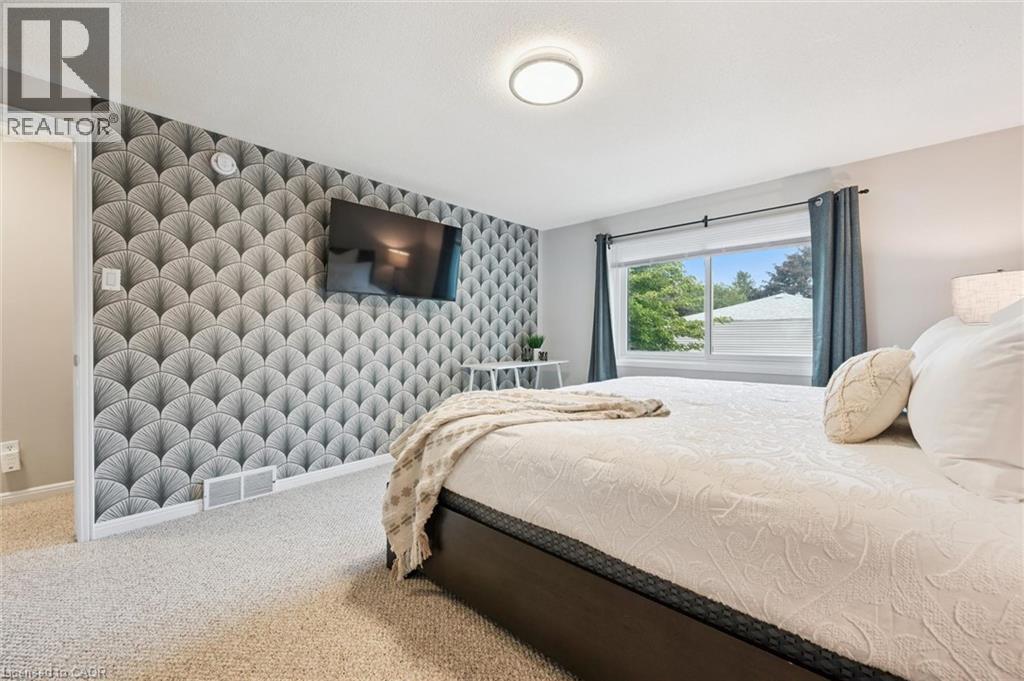 Textured accent wall, ceiling-mounted light fixture, light-toned carpeting, and a window with exterior views - 21 Colebrook Court, Kitchener, ON