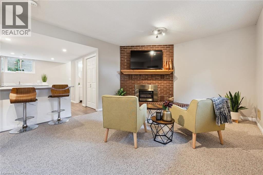 Carpeted living area featuring a brick fireplace with a wood mantel, an integrated bar with a solid surface countertop, recessed lighting, and a white paneled door - 21 Colebrook Court, Kitchener, ON