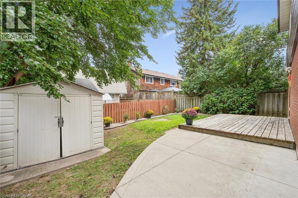 Fenced backyard featuring a concrete patio, wood deck, and a storage shed - 21 Colebrook Court, Kitchener, ON