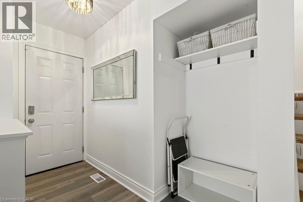 Entryway featuring a decorative ceiling light fixture, wood-finish flooring, and a built-in storage bench with an upper shelf - 27 Gretna Court, Hamilton, ON