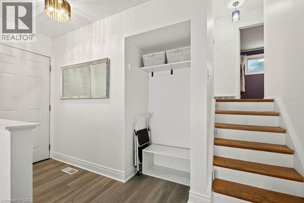 Entryway featuring wood-finish flooring, a built-in storage bench, and a modern drum light fixture - 27 Gretna Court, Hamilton, ON