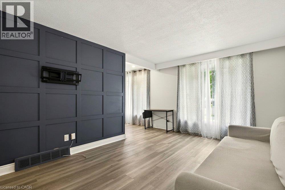 Accent wall with paneling, wood-finish flooring, and multiple windows - 27 Gretna Court, Hamilton, ON