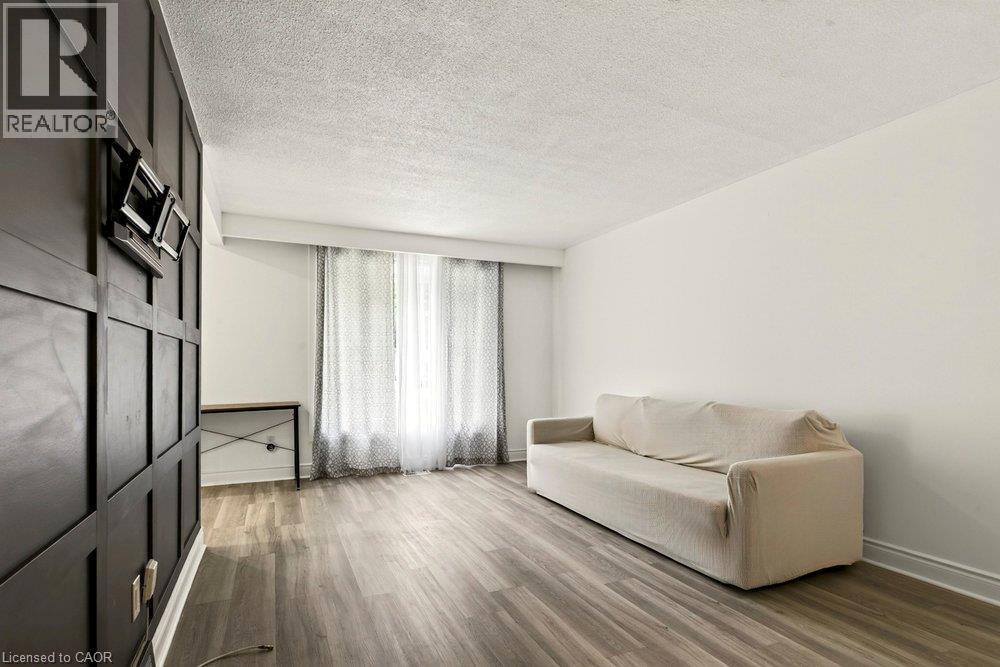 Wood-finish flooring throughout, complemented by a decorative paneled accent wall and white painted walls - 27 Gretna Court, Hamilton, ON