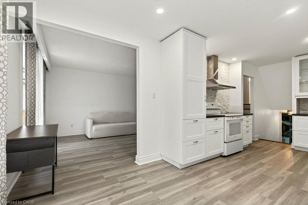 Recessed lighting, wood-finish flooring, white cabinetry, dark countertops, and a tile backsplash - 27 Gretna Court, Hamilton, ON