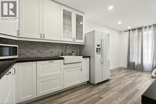 White shaker cabinetry, dark countertops, stacked stone backsplash, farmhouse sink, and wood-finish flooring - 27 Gretna Court, Hamilton, ON 