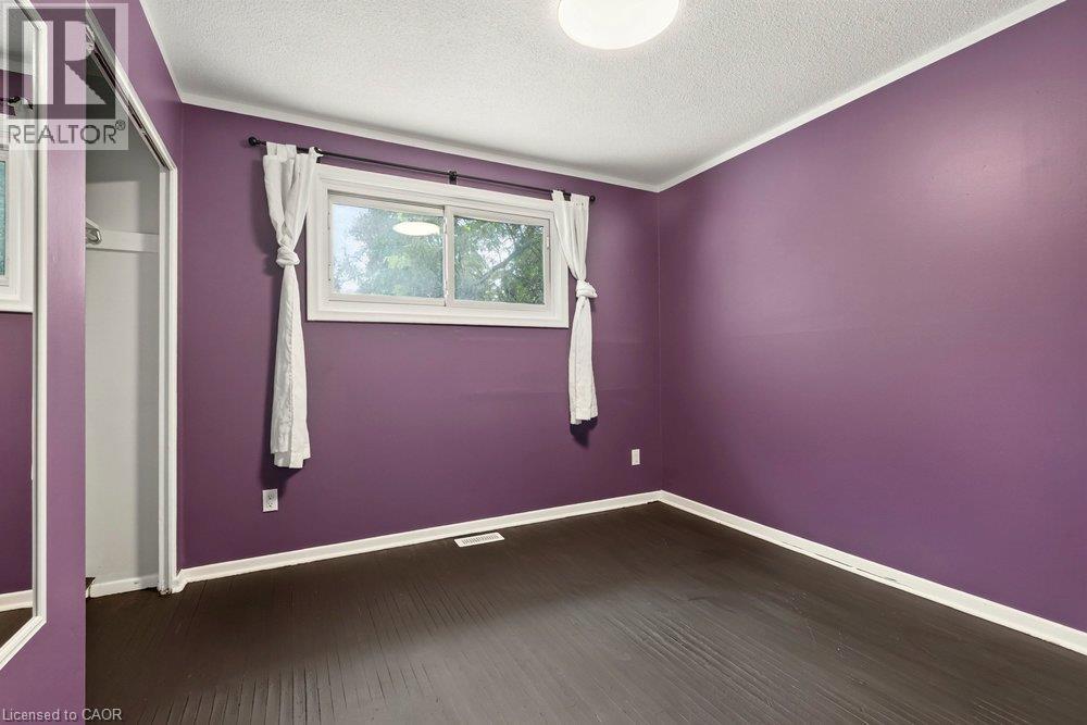 Dark wood-finish flooring with white trim, a single window, and a built-in closet with mirrored sliding doors - 27 Gretna Court, Hamilton, ON