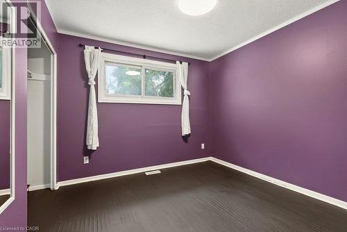 Dark wood-finish flooring with white trim, a single window, and a built-in closet with mirrored sliding doors - 27 Gretna Court, Hamilton, ON 
