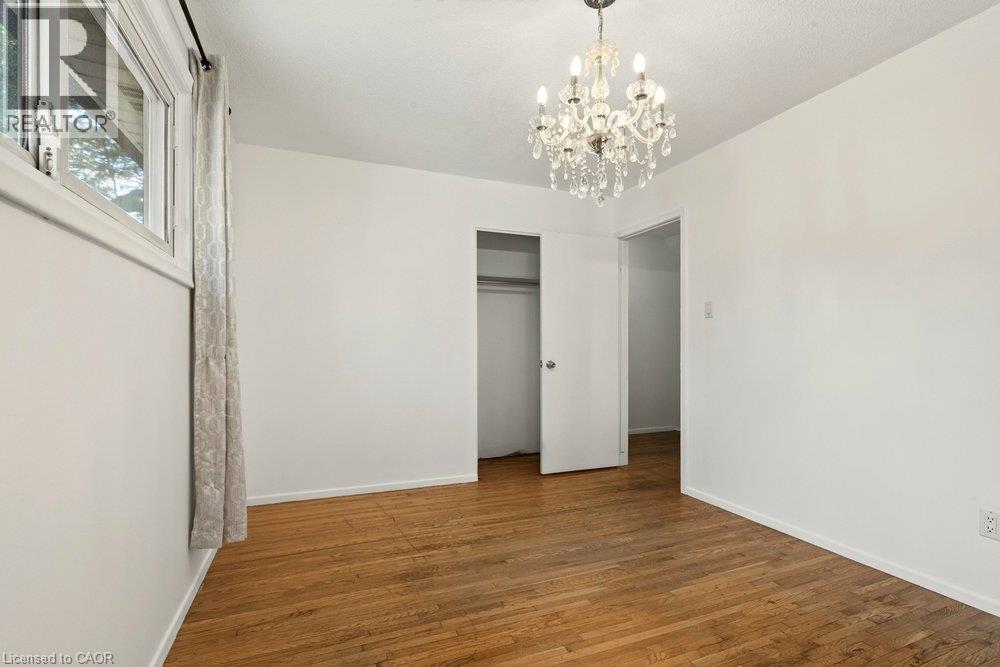 Wood-finish flooring with white walls, a crystal chandelier, and a window with trim - 27 Gretna Court, Hamilton, ON