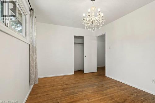 Wood-finish flooring with white walls, a crystal chandelier, and a window with trim - 27 Gretna Court, Hamilton, ON 