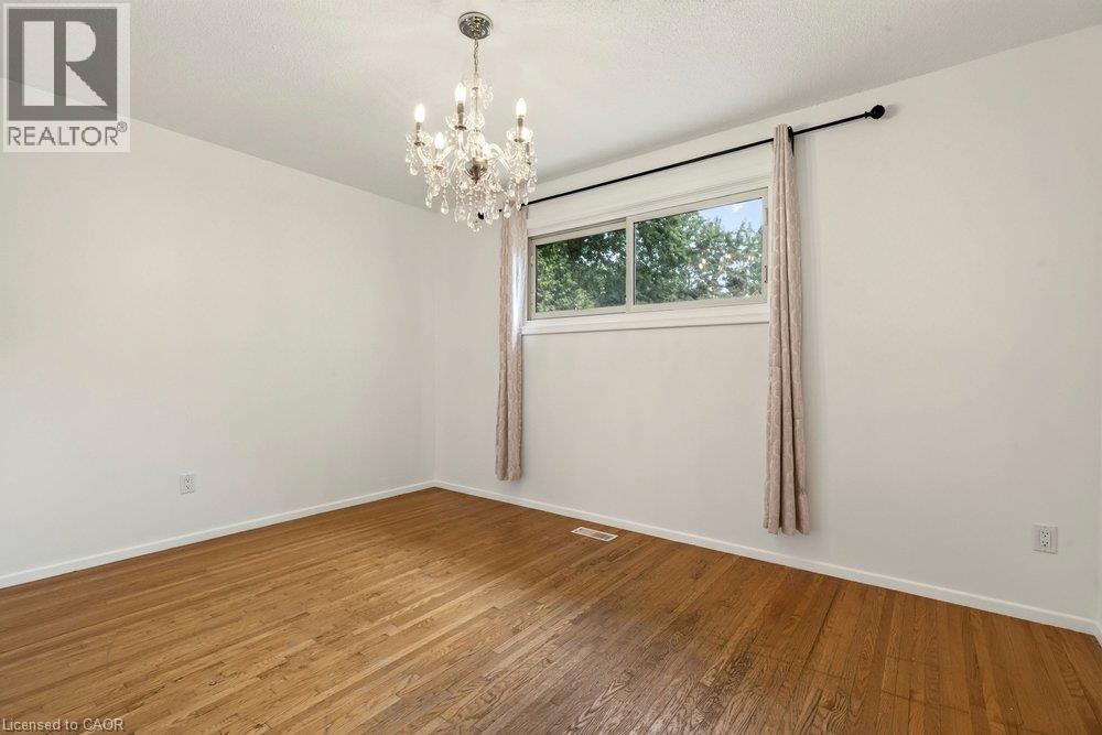 Hardwood flooring, crystal chandelier, white walls, and a window with a black curtain rod - 27 Gretna Court, Hamilton, ON