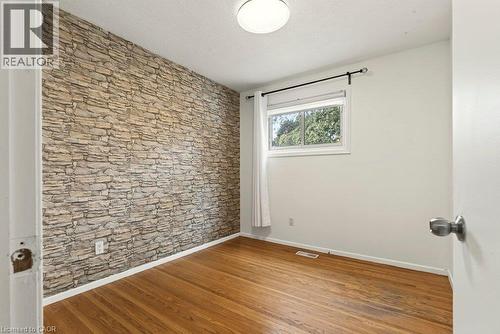 Stone accent wall, wood-finish flooring, and a flush mount ceiling light - 27 Gretna Court, Hamilton, ON 