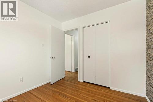 Hardwood flooring, white walls, white bi-fold closet doors, white interior door, and a stone accent wall - 27 Gretna Court, Hamilton, ON 
