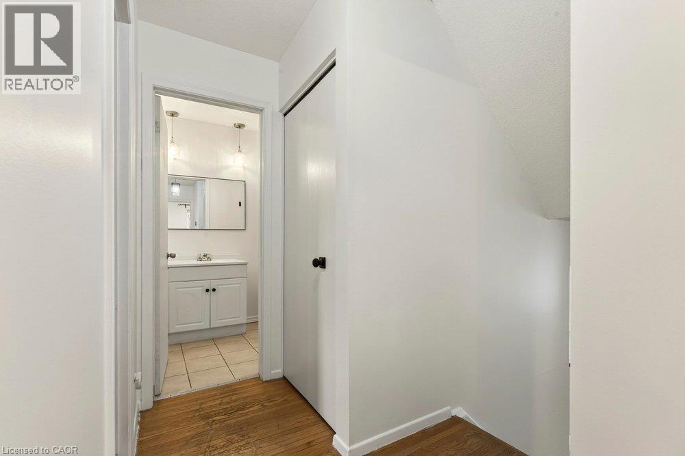 Wood-finish flooring with white baseboards, a white painted wall, and a built-in closet with a black door knob - 27 Gretna Court, Hamilton, ON