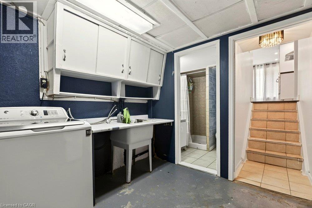 Laundry area with white cabinetry, utility sink, and overhead fluorescent lighting - 27 Gretna Court, Hamilton, ON