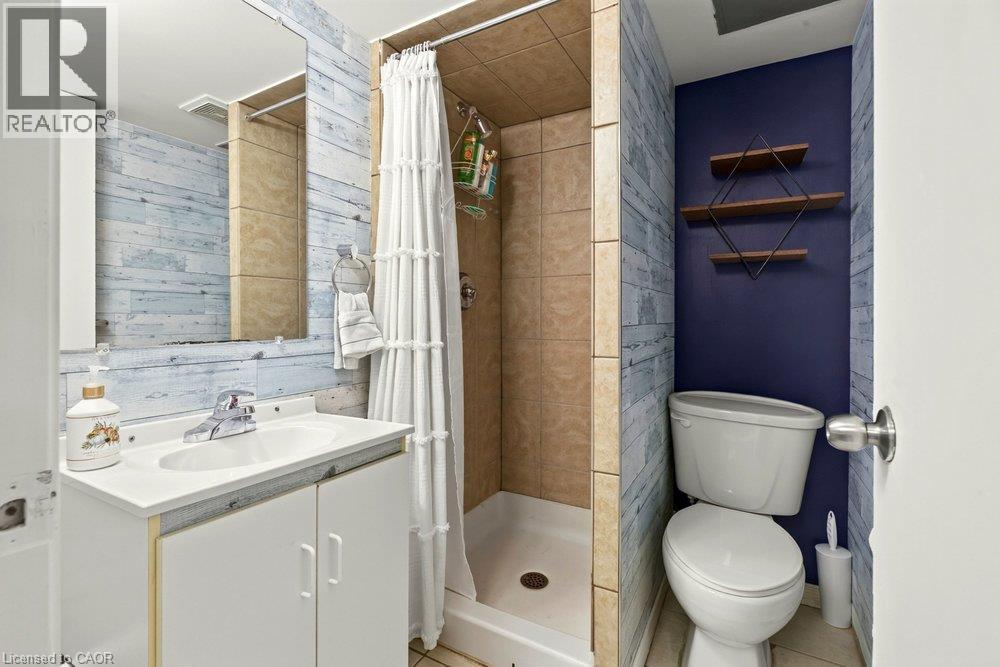 Bathroom featuring a white vanity with integrated sink, chrome faucet, wall-mounted mirror, and a stand-up shower with tiled walls - 27 Gretna Court, Hamilton, ON