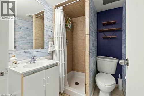 Bathroom featuring a white vanity with integrated sink, chrome faucet, wall-mounted mirror, and a stand-up shower with tiled walls - 27 Gretna Court, Hamilton, ON 