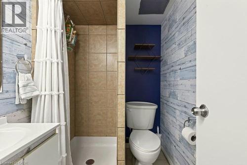 Tiled shower stall, white ceramic sink, wood-finish accent wall, and built-in shelving - 27 Gretna Court, Hamilton, ON 
