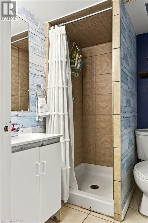 Shower with tile surround, white shower base, and adjacent vanity with white cabinetry - 27 Gretna Court, Hamilton, ON