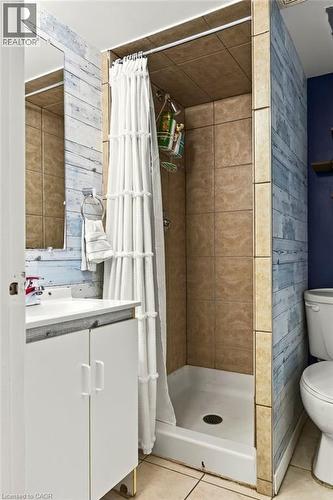 Shower with tile surround, white shower base, and adjacent vanity with white cabinetry - 27 Gretna Court, Hamilton, ON 