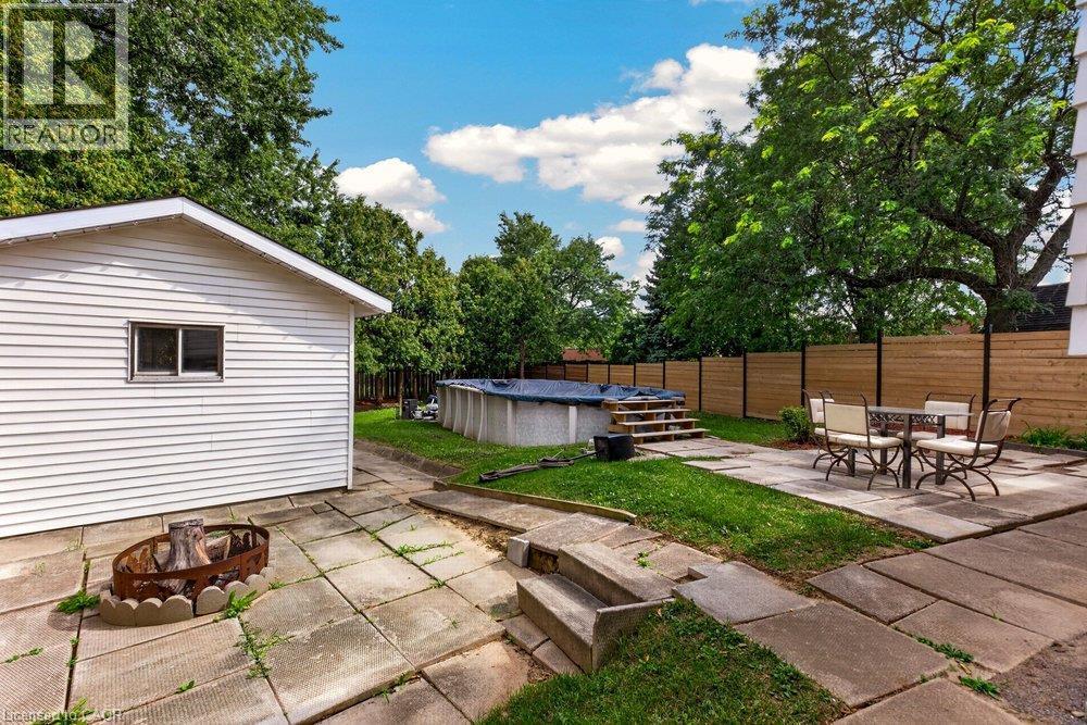 Backyard featuring an above-ground pool with stairs, a patio with concrete pavers, a fire pit area, and a horizontal slatted privacy fence - 27 Gretna Court, Hamilton, ON