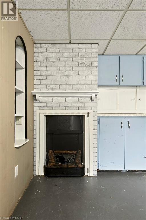 Whitewashed brick fireplace featuring a decorative mantel, built-in arched shelving, and overhead cabinetry - 27 Gretna Court, Hamilton, ON