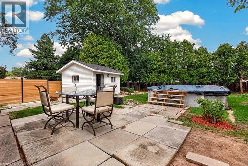 Expansive outdoor patio with large paver stones, a white storage shed with dark roof, and a privacy fence - 27 Gretna Court, Hamilton, ON 