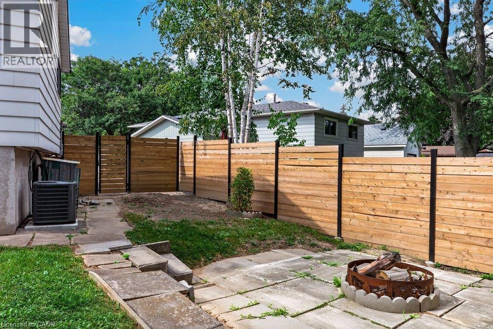Patio area featuring concrete pavers, wood fencing with black posts, and a stone-ringed fire pit - 27 Gretna Court, Hamilton, ON