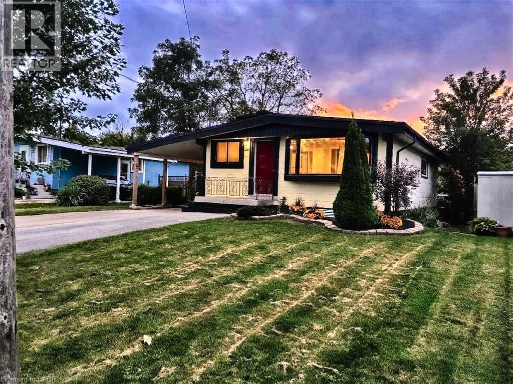 Front exterior featuring a covered carport, decorative front door, bay window, landscaped planting beds, and a front lawn - 134 Deschene Avenue, Hamilton, ON