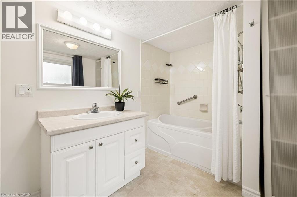 Bathroom featuring a white vanity with a light-toned countertop, a built-in tub, tiled shower surround, and light-toned floor tiling - 77 Beverly Street, Cambridge, ON