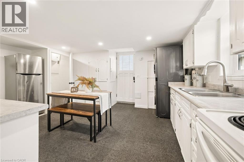 Compact kitchen featuring stainless steel refrigerator, white cabinetry, dual basin sink with a high-arc faucet, white electric range, and dark-toned flooring - 77 Beverly Street, Cambridge, ON
