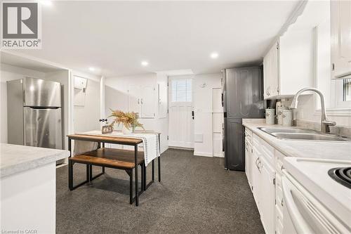 Compact kitchen featuring stainless steel refrigerator, white cabinetry, dual basin sink with a high-arc faucet, white electric range, and dark-toned flooring - 77 Beverly Street, Cambridge, ON 