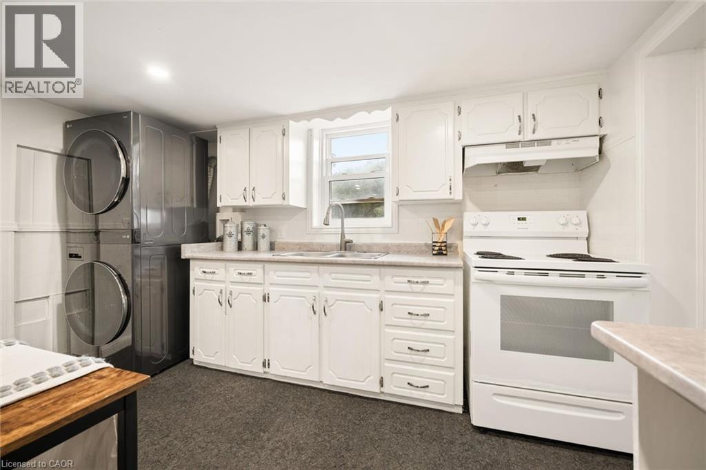 White cabinetry, light-toned countertops, stainless steel sink, white electric range, and stacked laundry appliances - 77 Beverly Street, Cambridge, ON