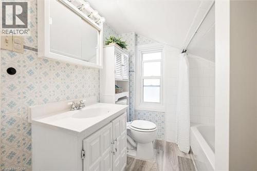 White vanity with integrated sink, patterned wall tile, wood-finish flooring, white built-in storage cabinet, and a bathtub with white subway tile surround - 77 Beverly Street, Cambridge, ON 