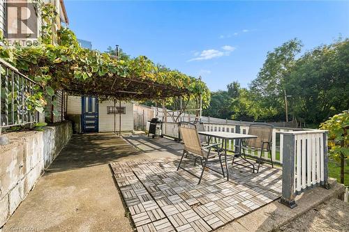 Outdoor patio area featuring a slatted wood-look floor, an overhead trellis with extensive foliage, a white picket fence, and a concrete retaining wall - 77 Beverly Street, Cambridge, ON 