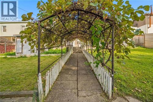 Picket fence bordering a concrete pathway, covered by a leafy overhead arbor - 77 Beverly Street, Cambridge, ON 