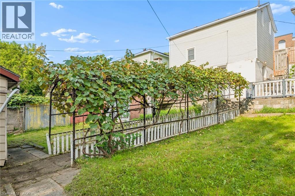 Rear exterior with white siding, a sloped lawn, a white picket fence, and a mature vine-covered arbor - 77 Beverly Street, Cambridge, ON