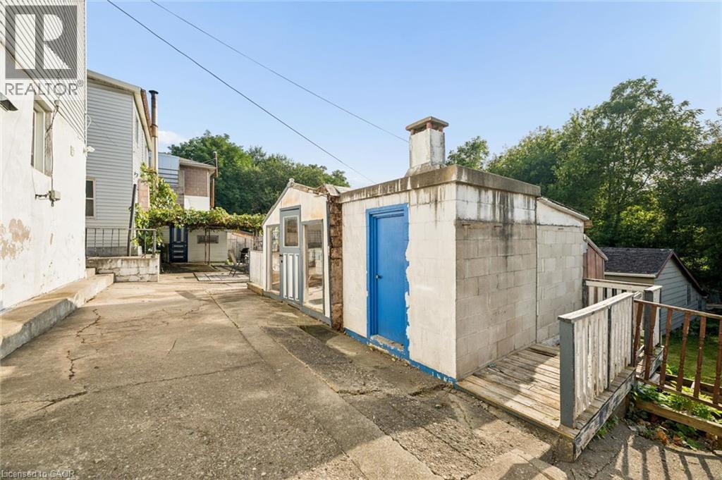 Concrete driveway with a detached block structure, a separate greenhouse-style building, and a wood-slat railing - 77 Beverly Street, Cambridge, ON