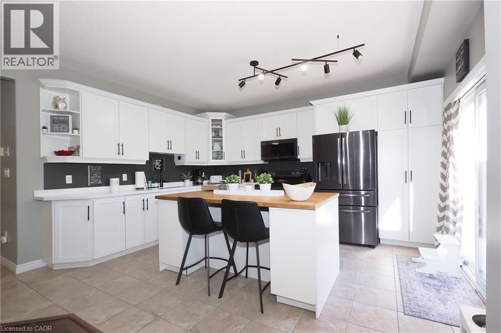 Modern kitchen featuring white cabinetry, a central island with a wood-finish countertop, stainless steel refrigerator, black built-in microwave, and track lighting - 1200 Dunbar Road, Cambridge, ON