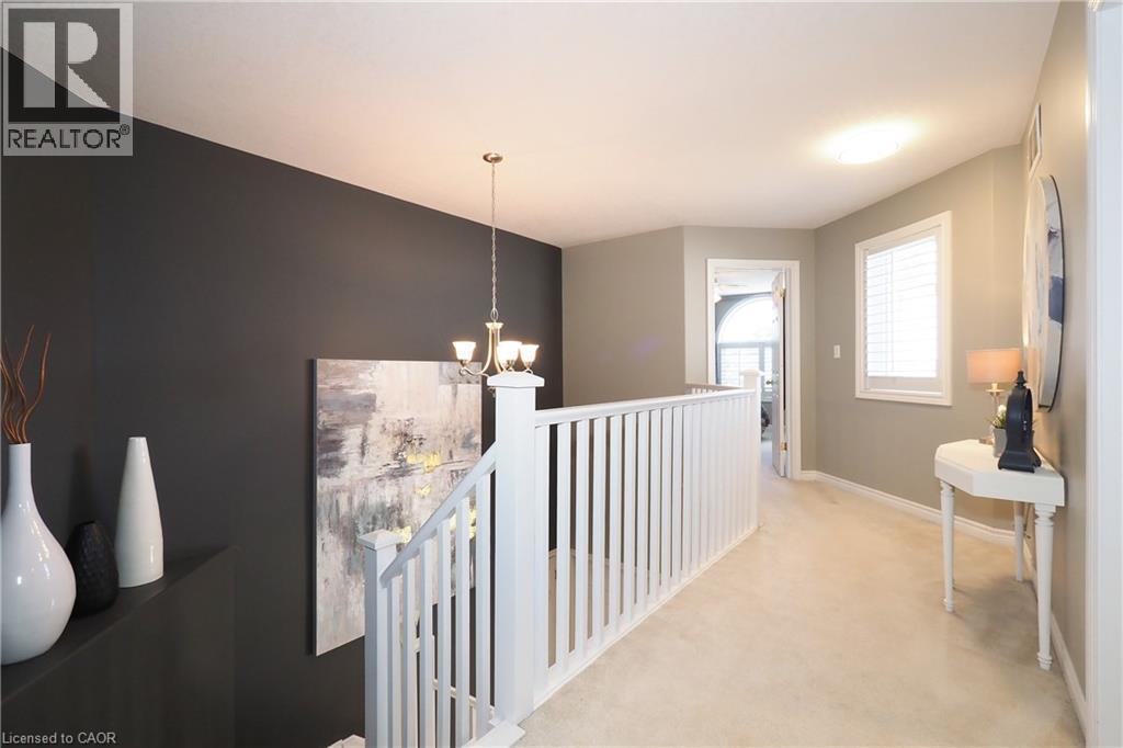 Upper-level hallway featuring a white baluster railing, neutral carpeting, a window with white shutters, and a brass-finish chandelier - 1200 Dunbar Road, Cambridge, ON